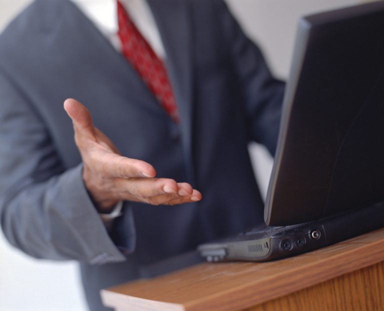Close-up of businessman's hand and laptop computer at podium