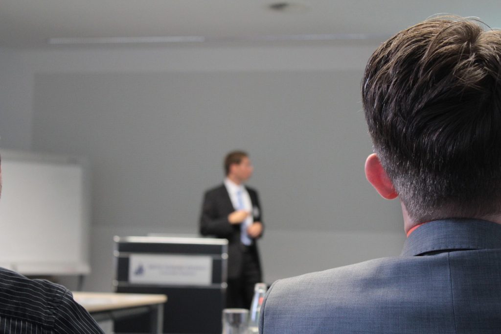 man giving a presentation in a classroom behind a lectern.