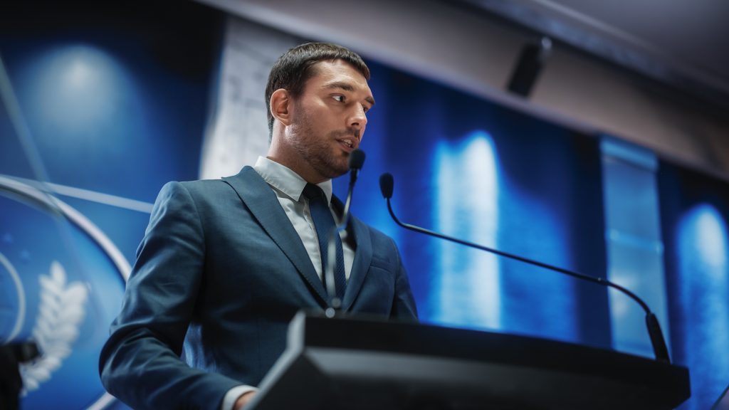 Portrait of an Young Organization Representative Speaking at an event behind a lectern and microphone.