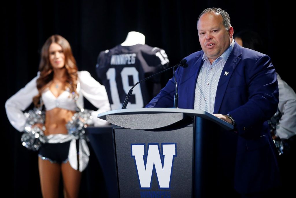 A man in a suit and tie speaking at a podium with cheerleaders standing behind him in support.