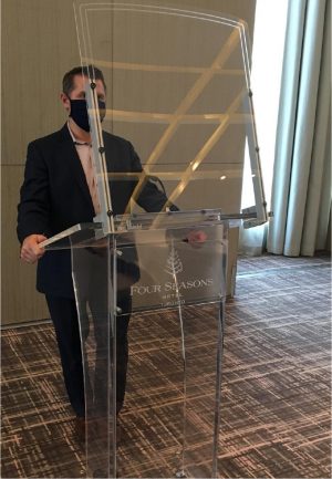 Asset-32@3xs-100.jpg Person wearing COVID-19 mask standing behind an acrylic lectern with an acrylic barrier attached